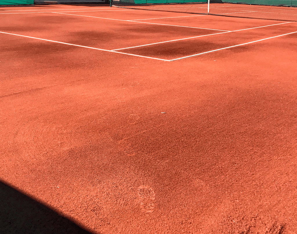 Brushing caliclay basalt into the turf during a red clay tennis court installation 1st layer